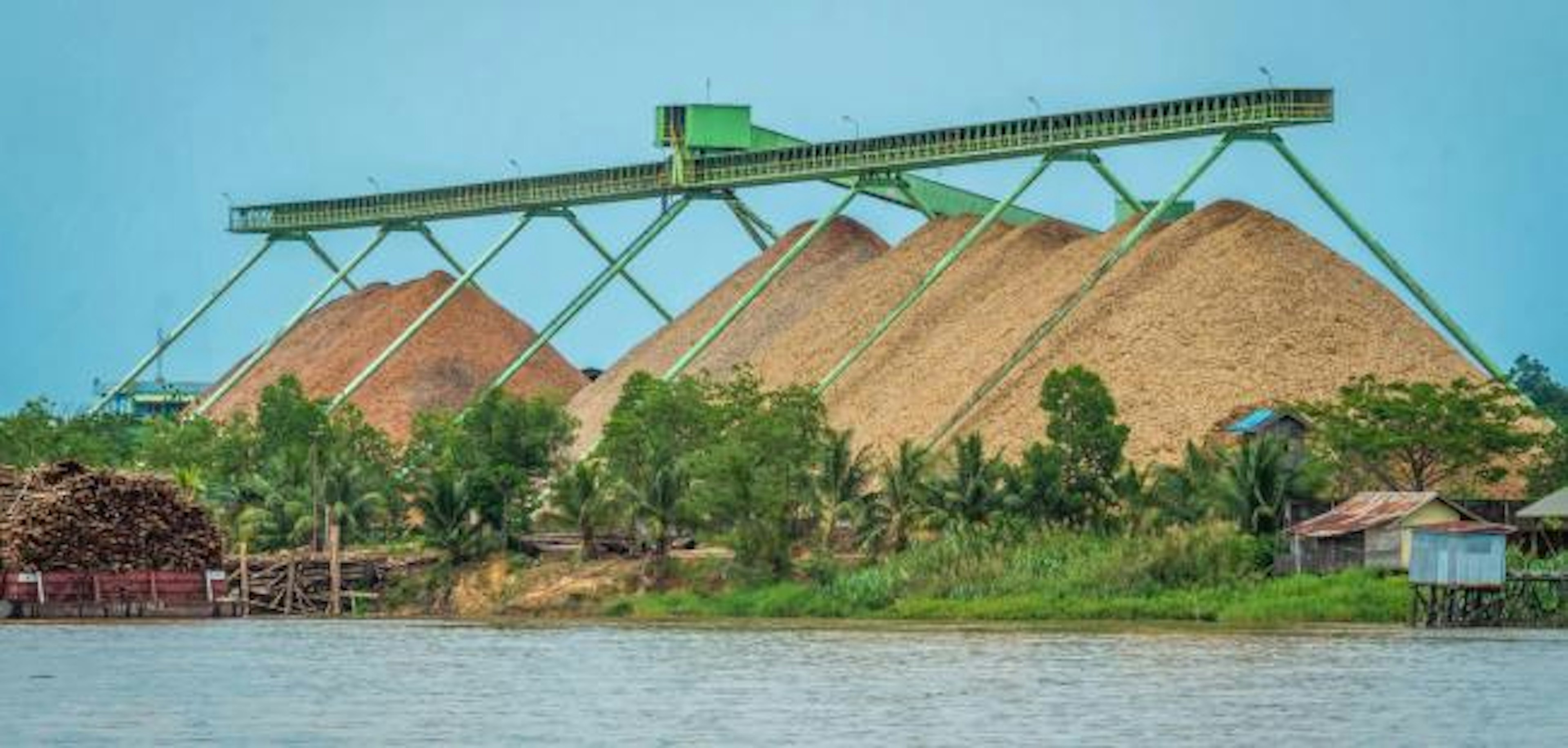 Wood chip factory on Mahakam riverbank with conveyor and stockpile, Indonesia